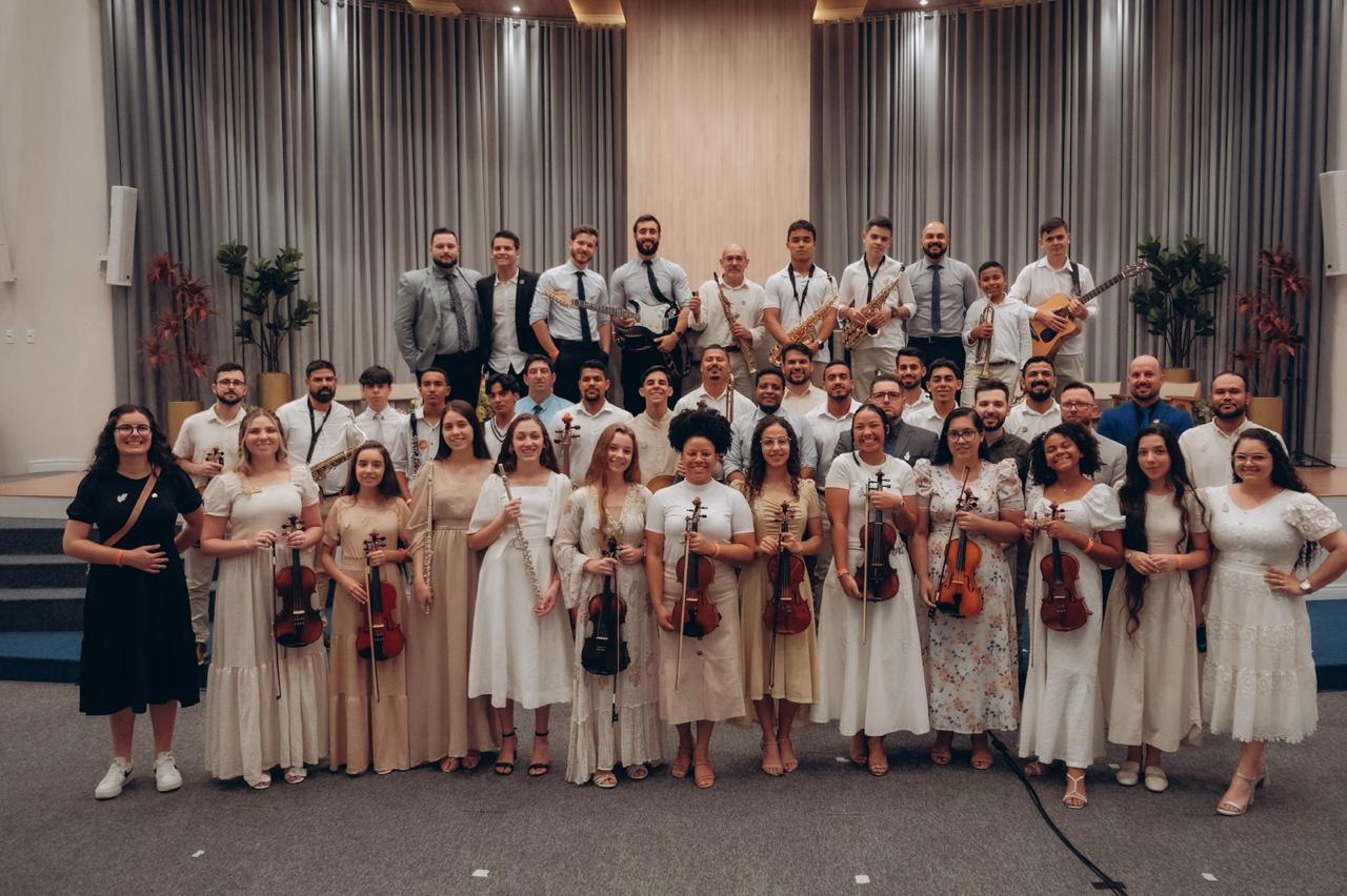 Músicos da Orquestra da Mensagem reunidos no palco, com instrumentos de cordas e sopros.